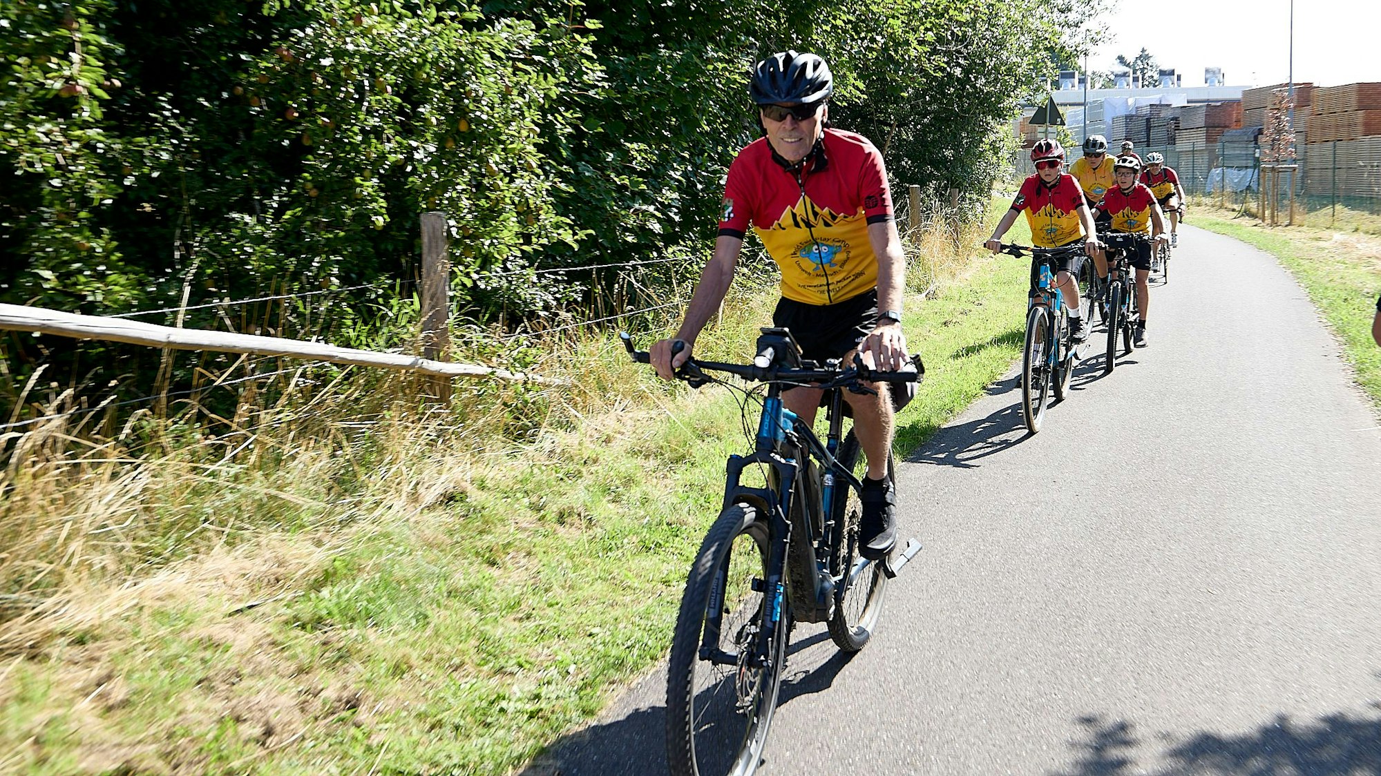 Die Radfahrer des Fair-Play-Camps fahren in rot-gelben Trikots in einer Reihe auf dem Radweg.