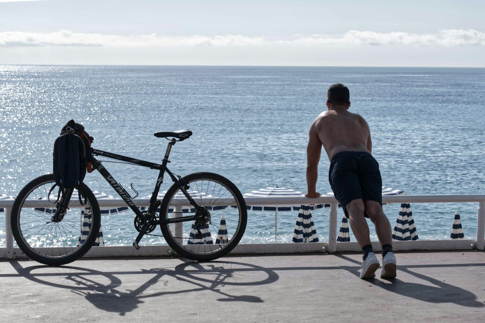 Ein Mann mit nacktem Oberkörper macht am Strand von Nizza neben seinem Fahrrad Übungen. (Archivbild)