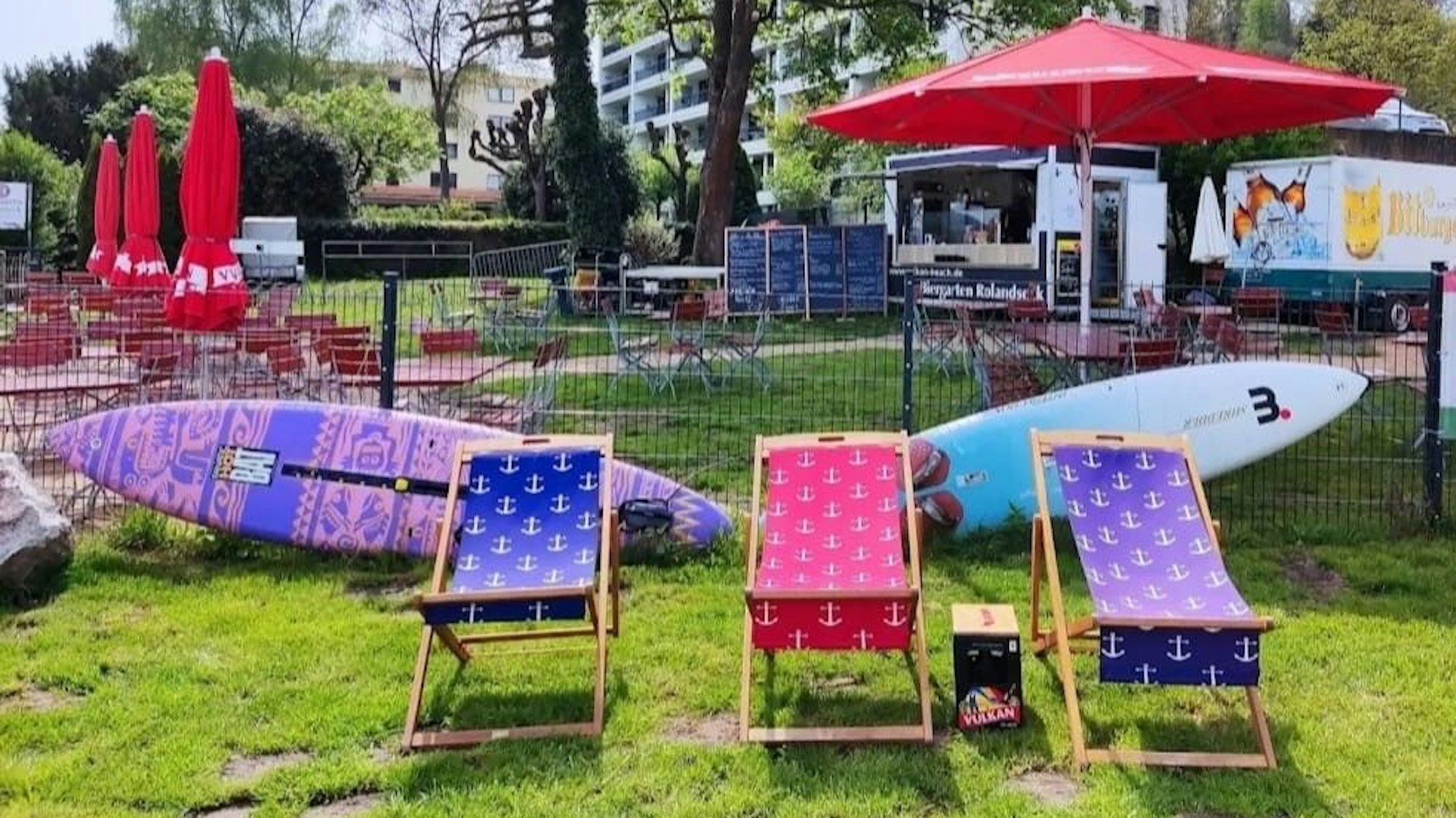 Liegestühle, Strandkörbe, und Bierbänke stehen nah am Wasser mit Blick auf das Siebengebirge.