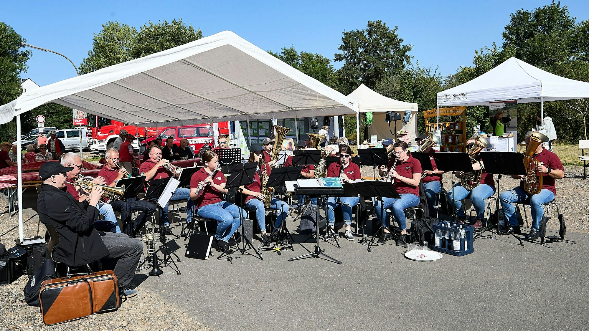 Die Musikerinnen und Musiker sitzen im Halbkreis unter weißen Zeltdächern.