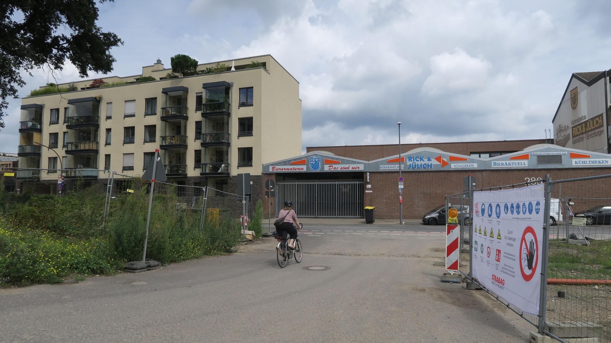 Bauzäune stehen links und rechts von einer Straßen-Einfahrt.
