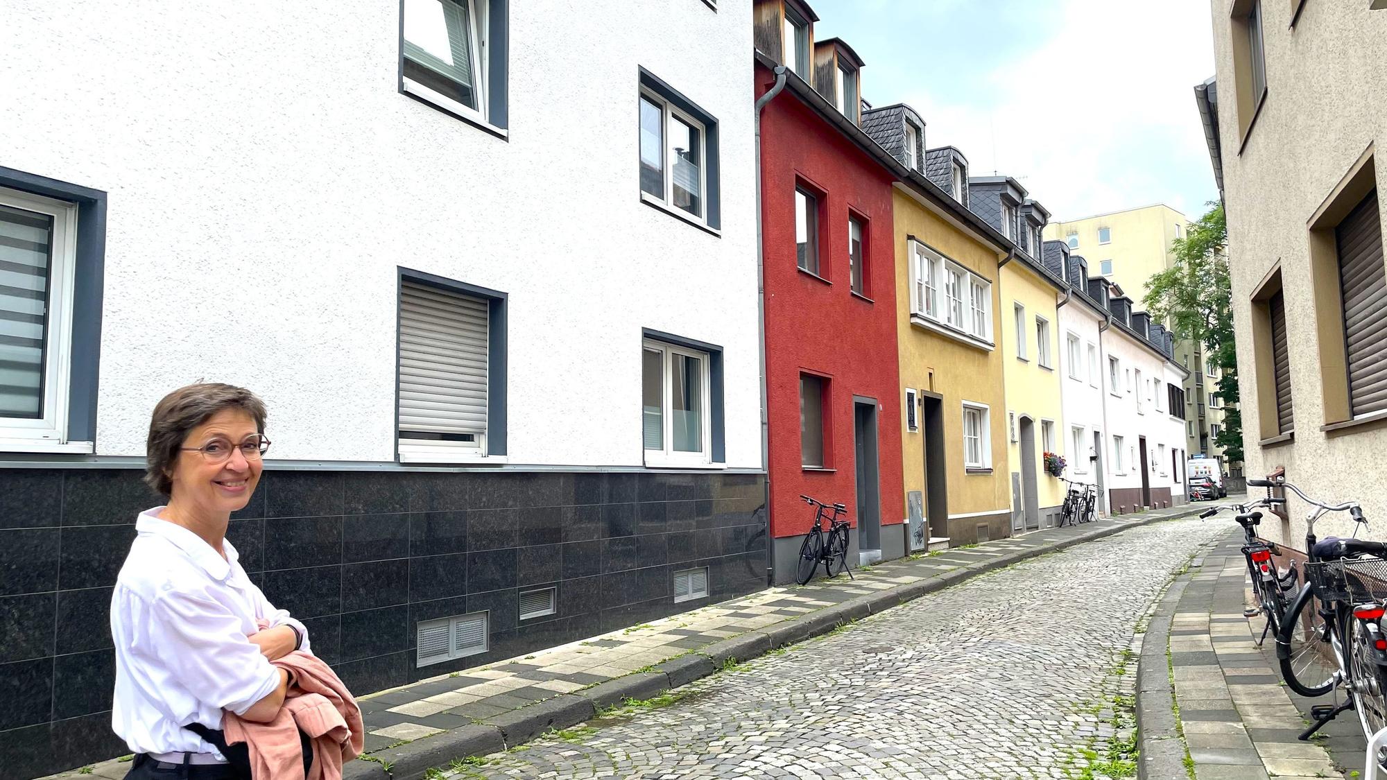 Eine Frau schaut in die Kamera, während sie durch eine schmale Straße geht.