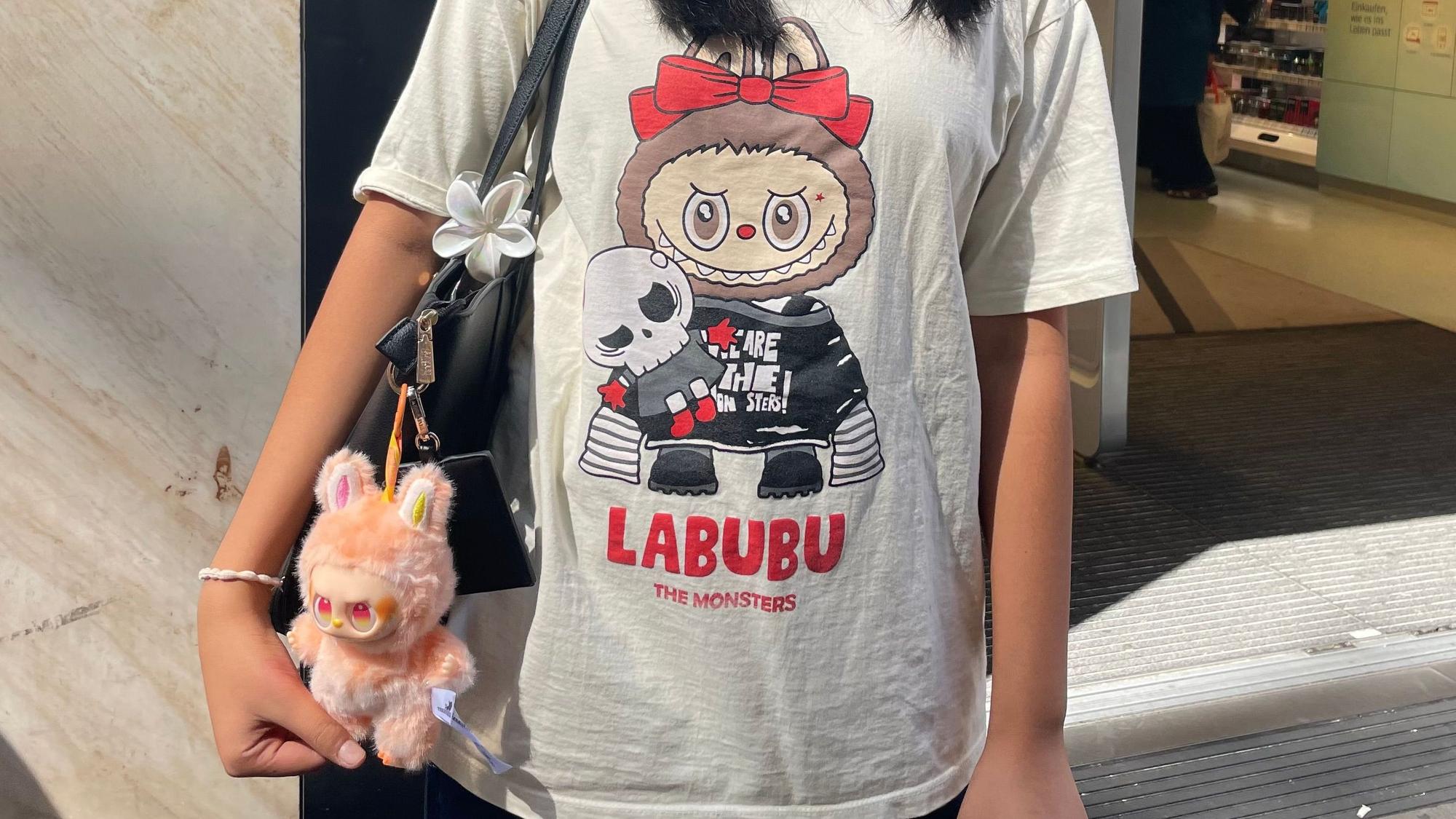 Ein Mädchen trägt ein Shirt mit einem Labubu-Aufdruck, an ihrer Tasche hängt ebenfalls ein Labubu.