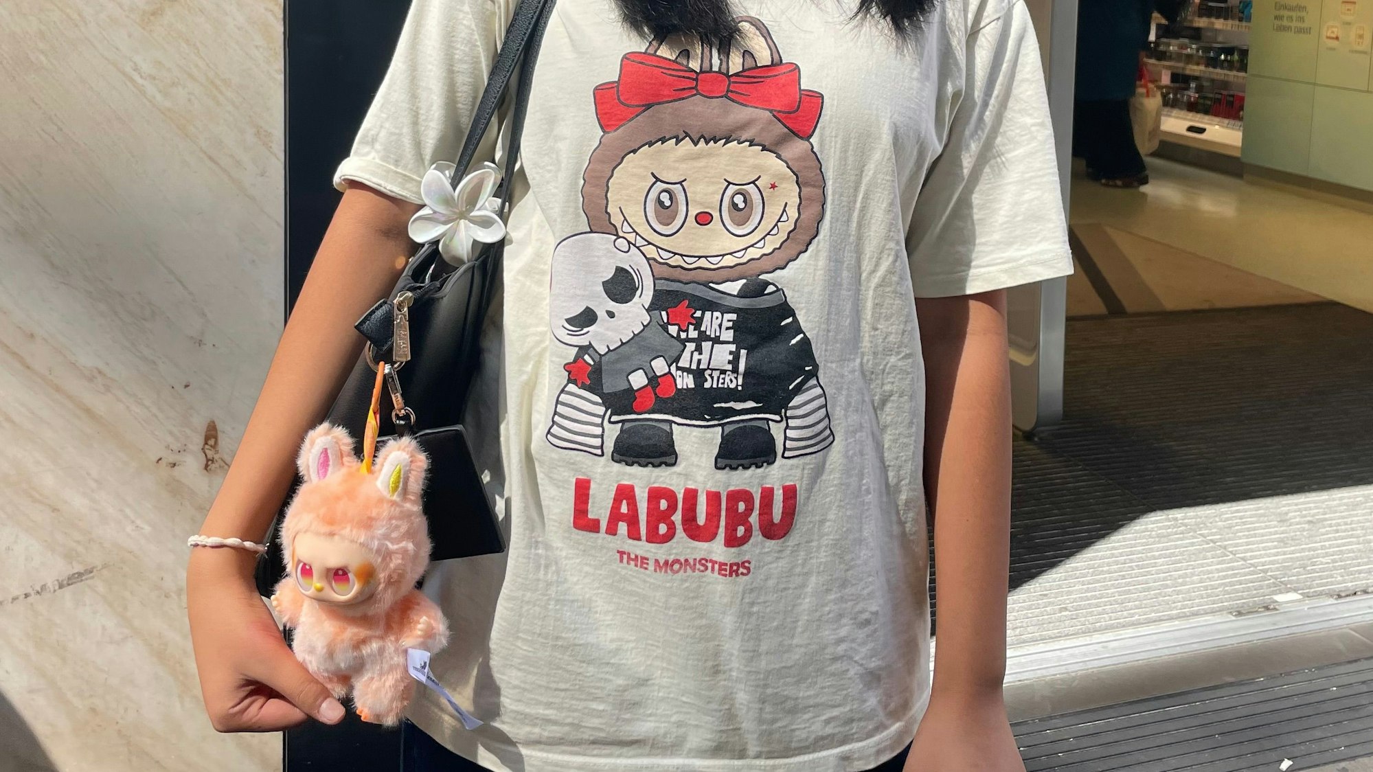 Ein Mädchen trägt ein Shirt mit einem Labubu-Aufdruck, an ihrer Tasche hängt ebenfalls ein Labubu.