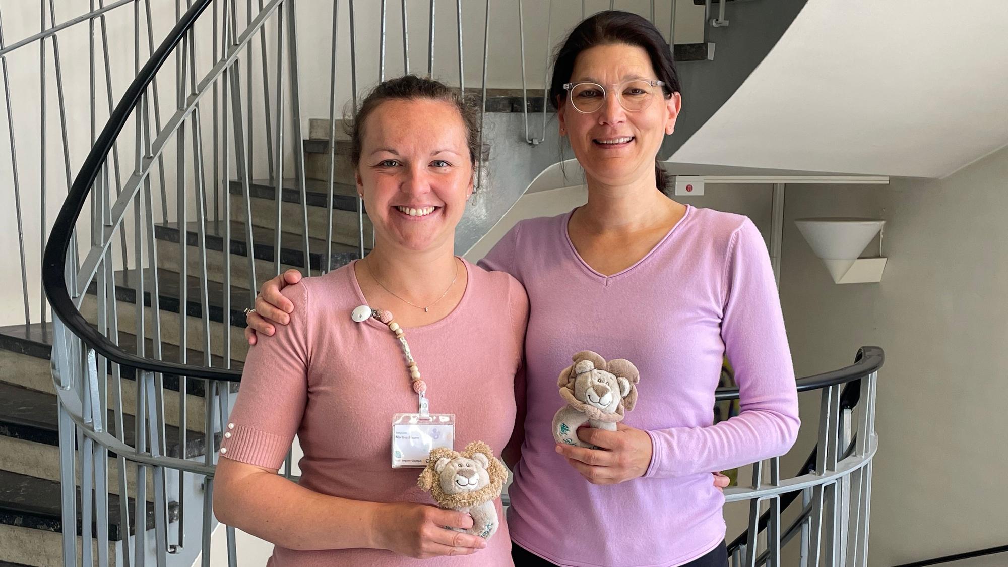 Babylotsin Martina Maurer (l.) und Netzwerkkoordinatorin Irene Rüttenauer stehen nebeneinander und halten Kuscheltiere in der Hand.