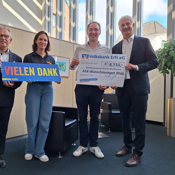 Eine Frau und drei Männer lächeln in die Kamera, zwei der Männer halten einen symbolischen Scheck über 6.750 Euro in den Händen.