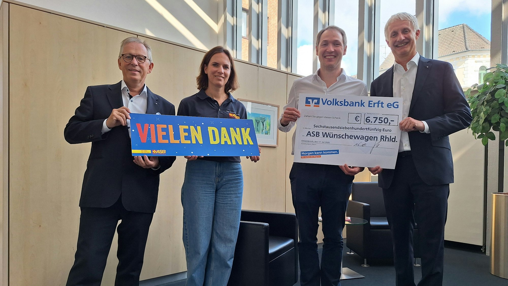 Eine Frau und drei Männer lächeln in die Kamera, zwei der Männer halten einen symbolischen Scheck über 6.750 Euro in den Händen.