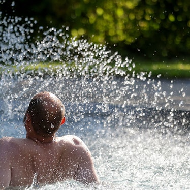 Das Bild zeigt einen Mann, der sich im Freibad an einem Wasserspiel erfrischt. Foto: Thomas Warnack/dpa