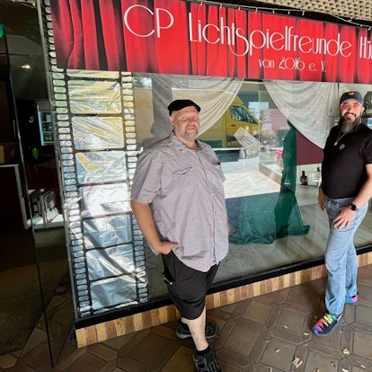 Die beiden Männer stehen vor einer Glasscheibe, darüber die Aufschrift: CP Lichtspielfreunde Hürth.