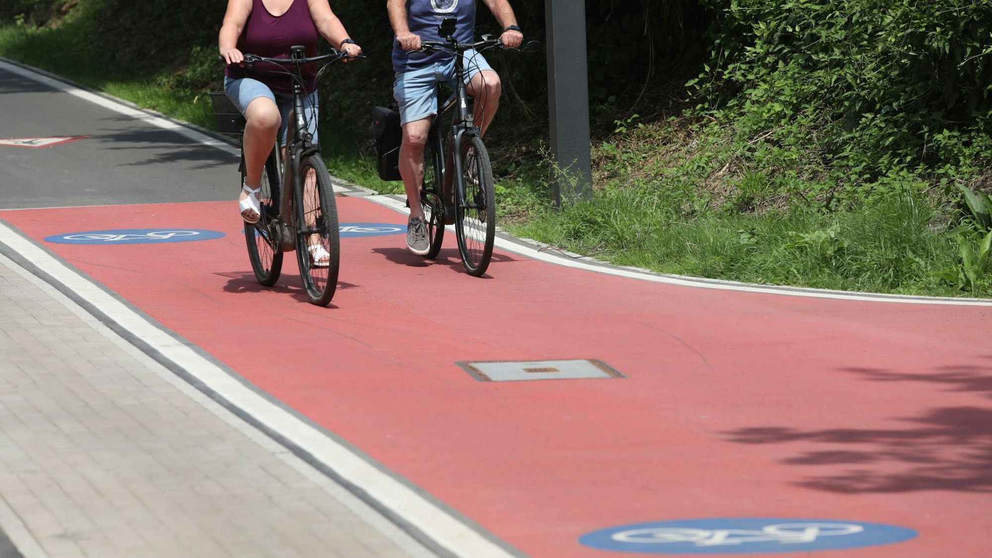 Zwei Radfahrer auf einem Radweg, der teilweise rot asphaltiert ist.