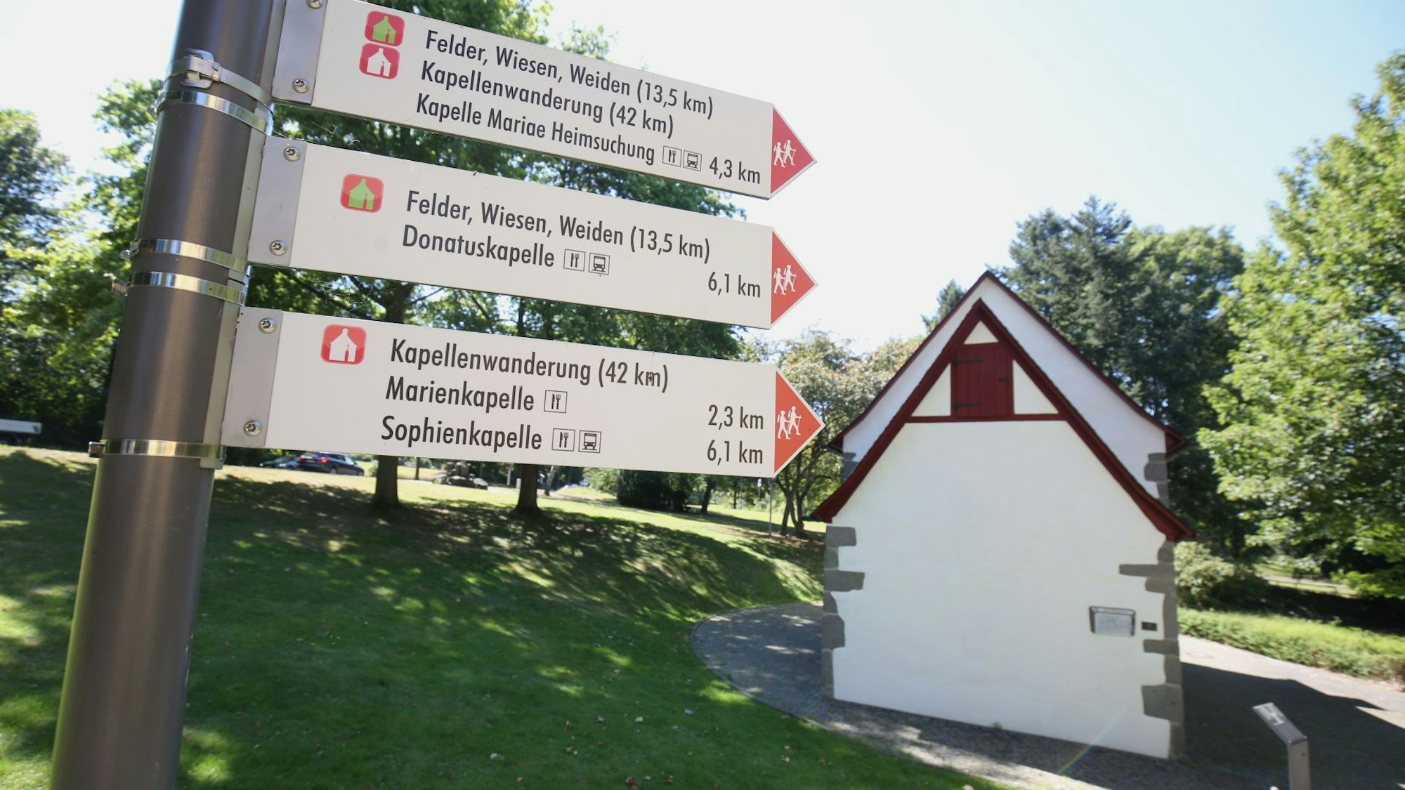 Schilder weisen den Weg für die Kapellenwanderung, im Hintergrund steht eine kleine Kapelle.