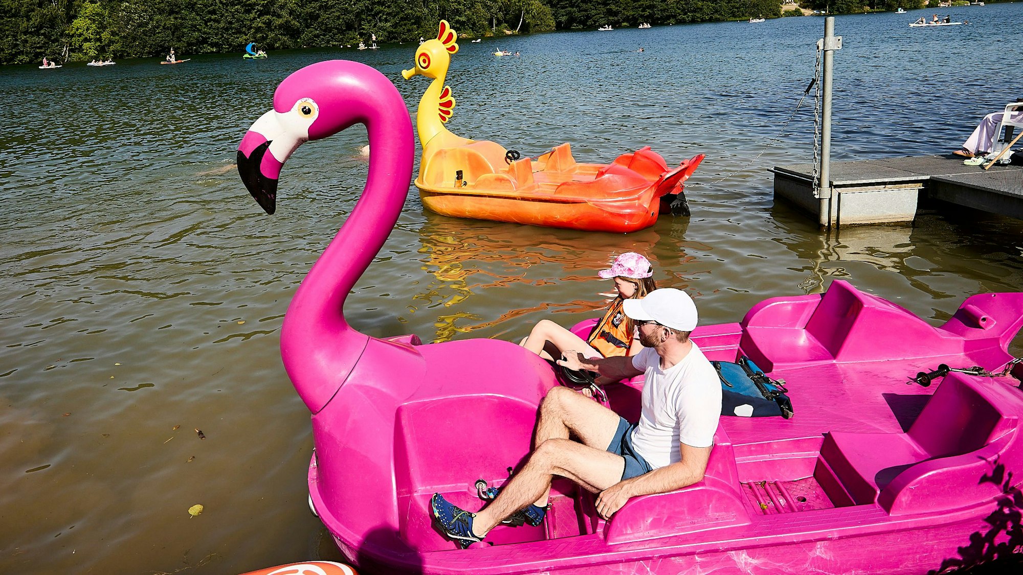 Ein Tretboot in der Form eines rosa Flamingos ist mit einem Vater und seiner kleinen Tochter besetzt.