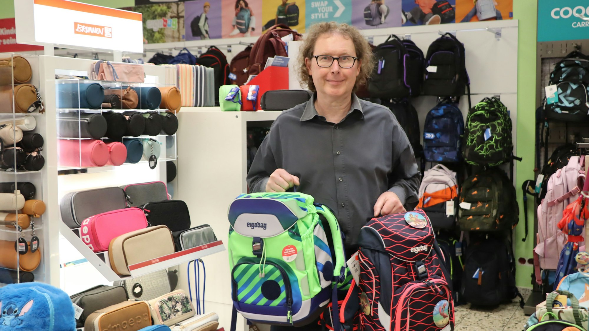 An Mann hält zwei Schulranzen in den Händen.