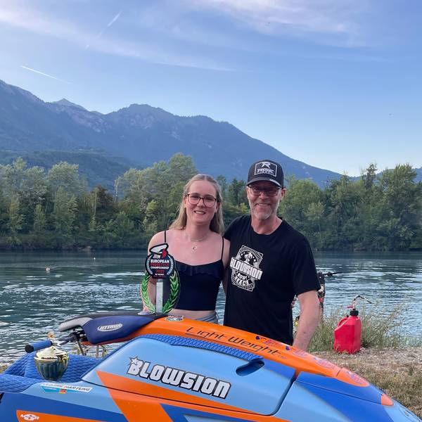 Eine junge Frau steht mit ihrem Vater hinter einem Jet-Ski und präsentiert ihren gewonnen Pokal.
