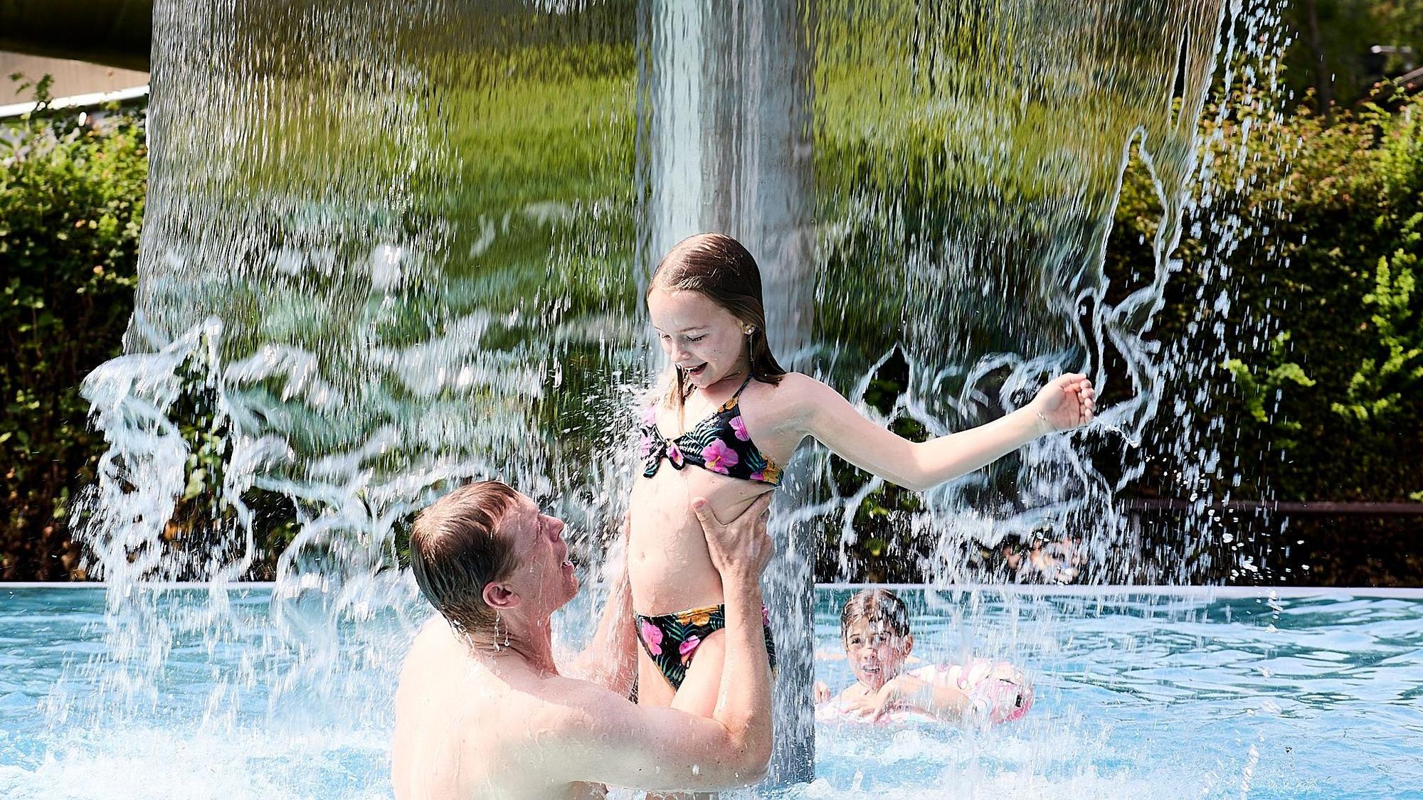 Ein Mann steht mit seiner Tochter im Freibad unter dem Wasserpilz.