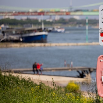 Ein Hinweisschild mit der Aufschrift „Achtung Lebensgefahr“ weist am Rhein in Köln-Rodenkirchen auf die Gefahren beim Schwimmen in dem Fluss hin.