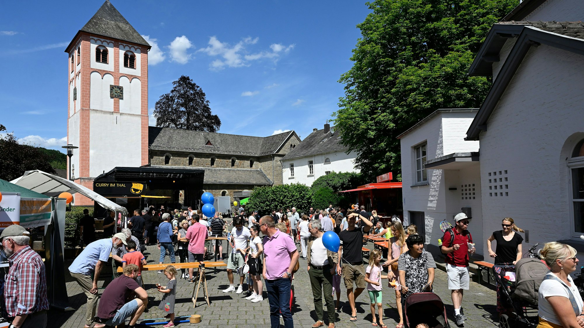 Viele Menschen feiern ein buntes Fest. Im Hintergrund der Turm einer Kirche.