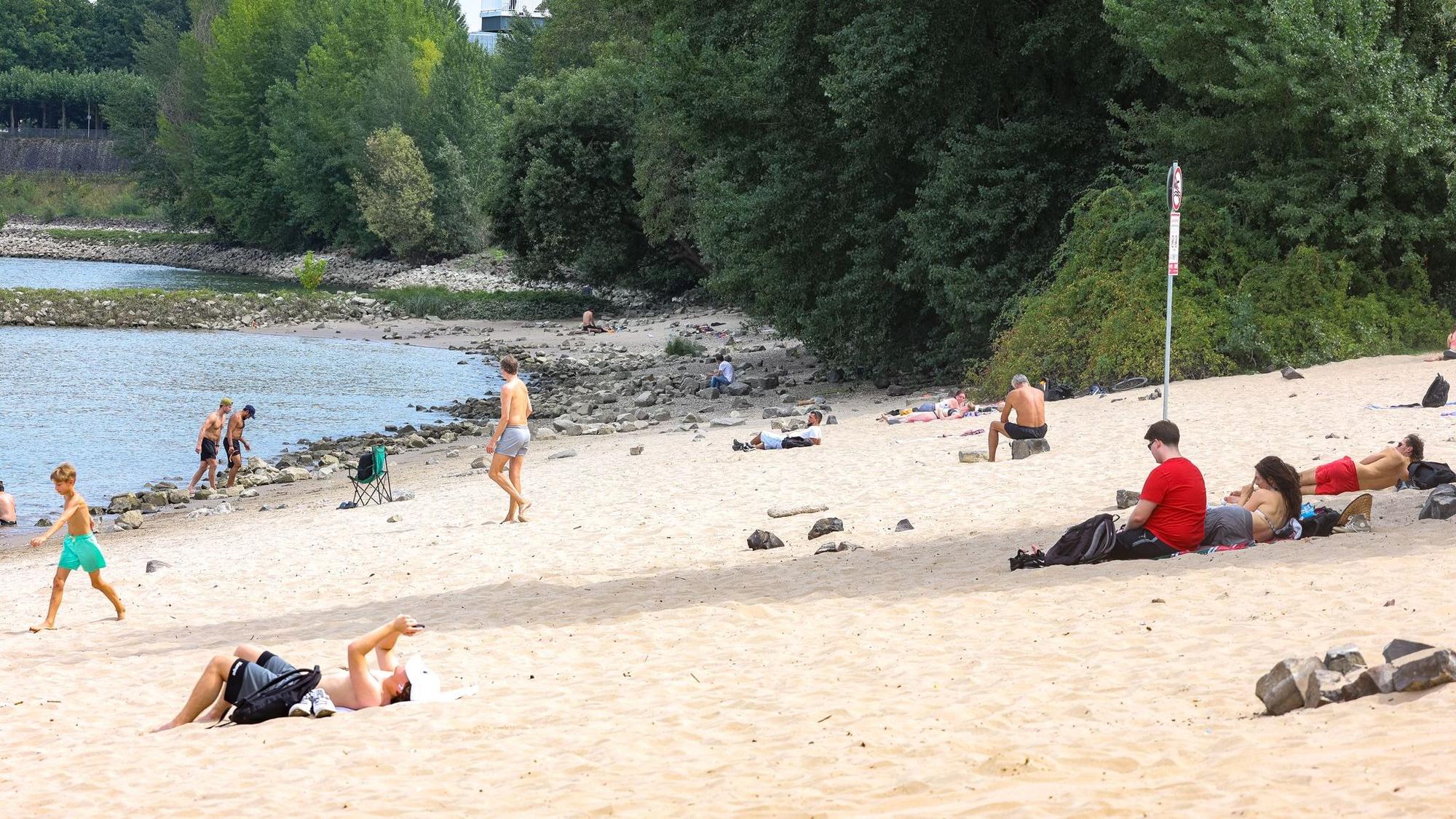 14.08.2025, Nordrhein-Westfalen, Düsseldorf: Menschen sitzen am Paradiesstrand am Rhein. In der nordrhein-westfälischen Landeshauptstadt gilt ab heute ein Badeverbot im Rhein.