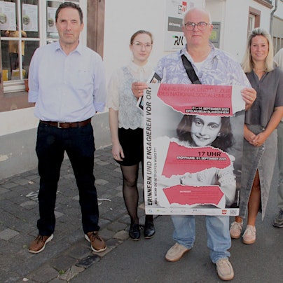 Drei Frauen und drei Männer, von denen einer ein Plakat hält, stehen vor dem Museum.