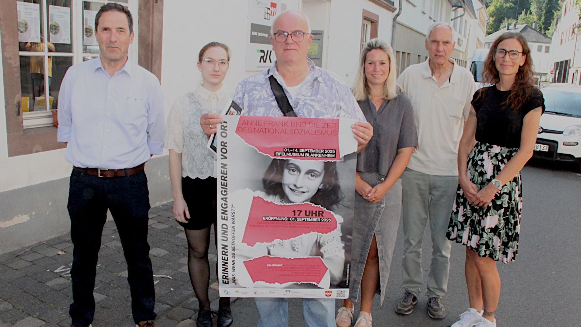 Drei Frauen und drei Männer, von denen einer ein Plakat hält, stehen vor dem Museum.