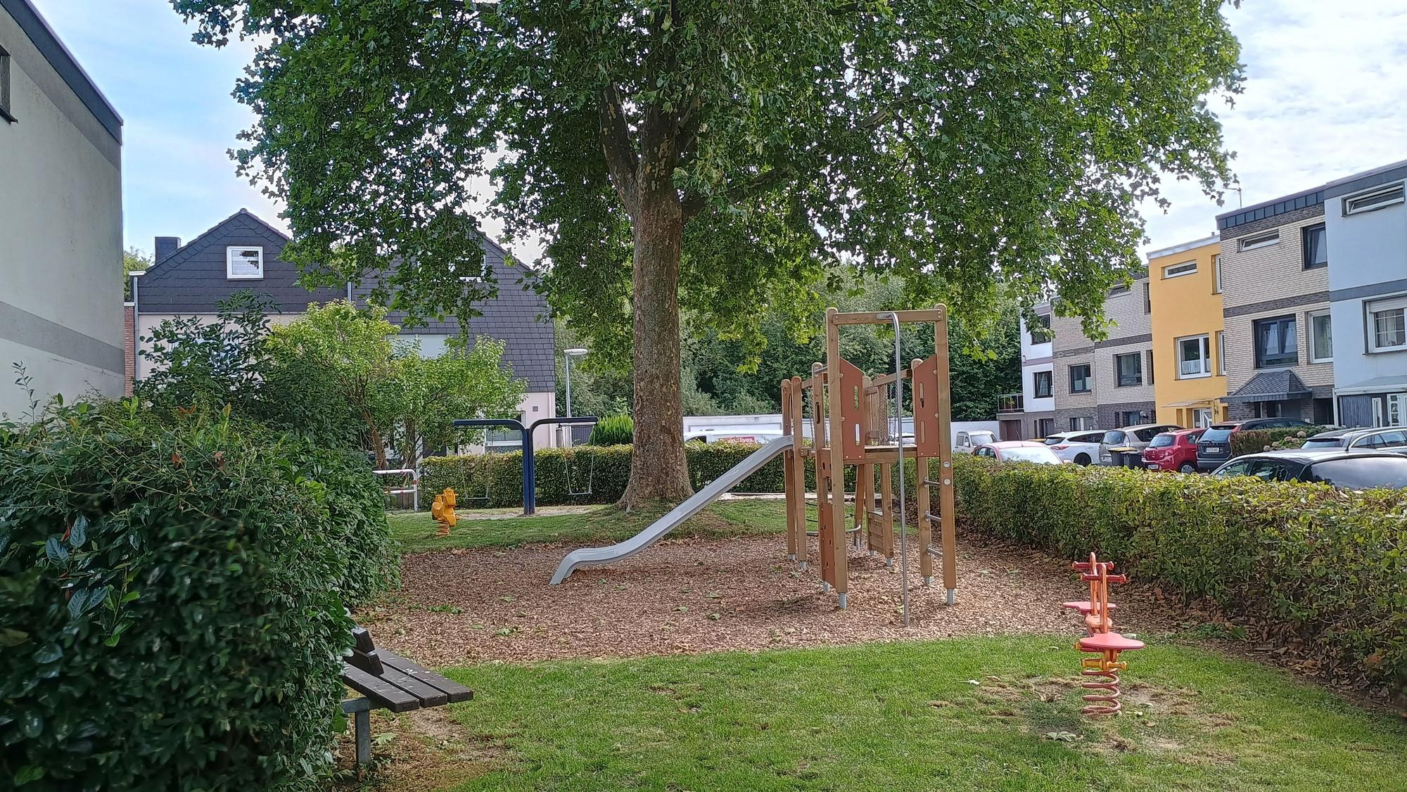 Das Bild zeigt den Spielplatz mit Rutsche und einer Bank sowie einen der beiden Schlafbäume.