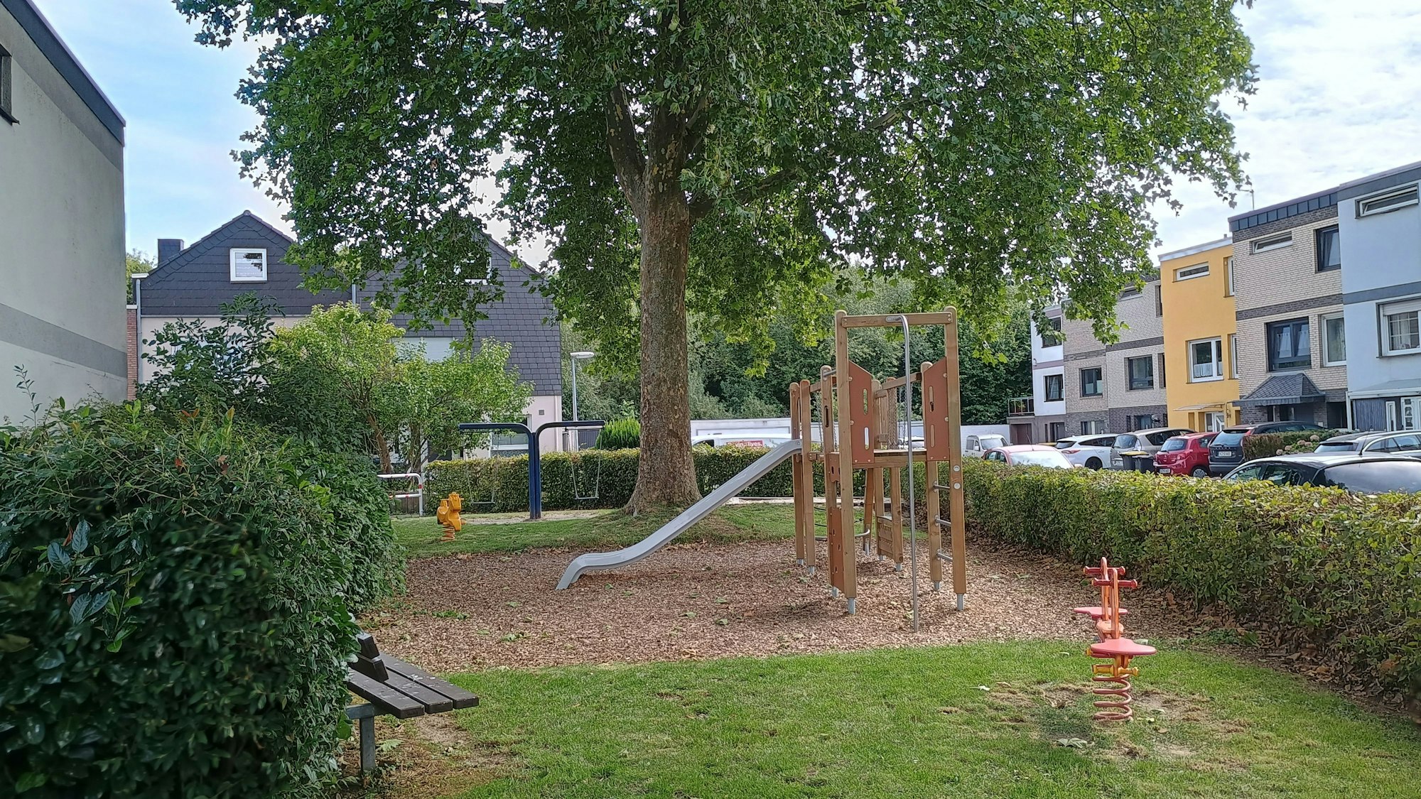 Das Bild zeigt den Spielplatz mit Rutsche und einer Bank sowie einen der beiden Schlafbäume.