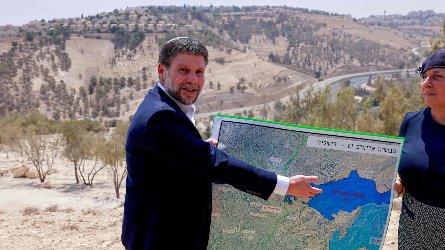 Bezalel Smotrich zeigt lächelnd auf eine Karte.