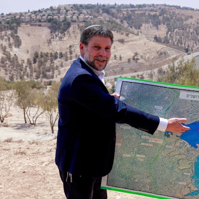 Bezalel Smotrich zeigt lächelnd auf eine Karte.