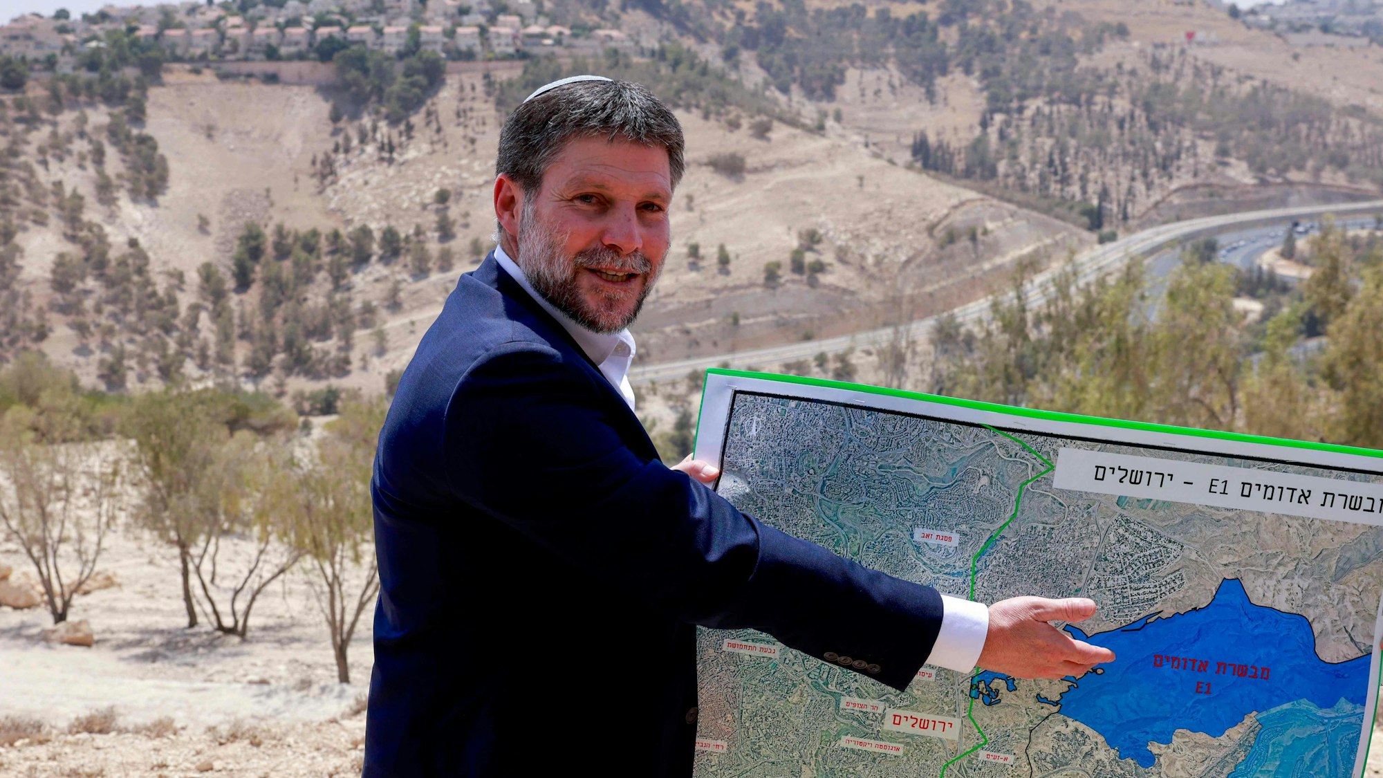 Bezalel Smotrich zeigt lächelnd auf eine Karte.