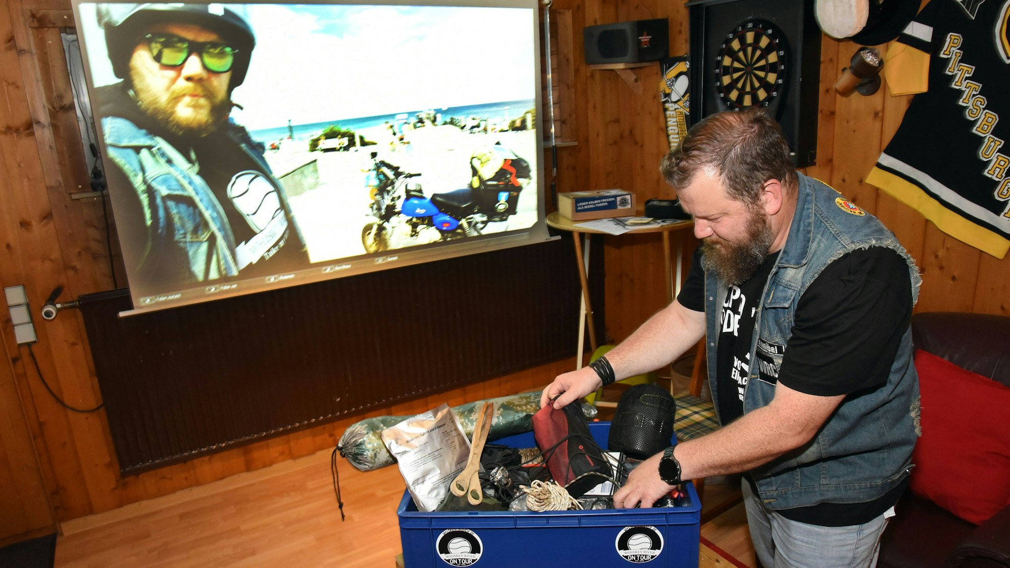 Manuel Krischer aus Wiehl-Drabenderhöhe hat sein Gepäck genau im Blick. Darin findet sich ein Zelt ebenso wie ein Faltgrill. Alles wird nachher umgeladen in eine Spezialbox. Im Hintergrund: Aufnahmen von der Ostsee-Tour.