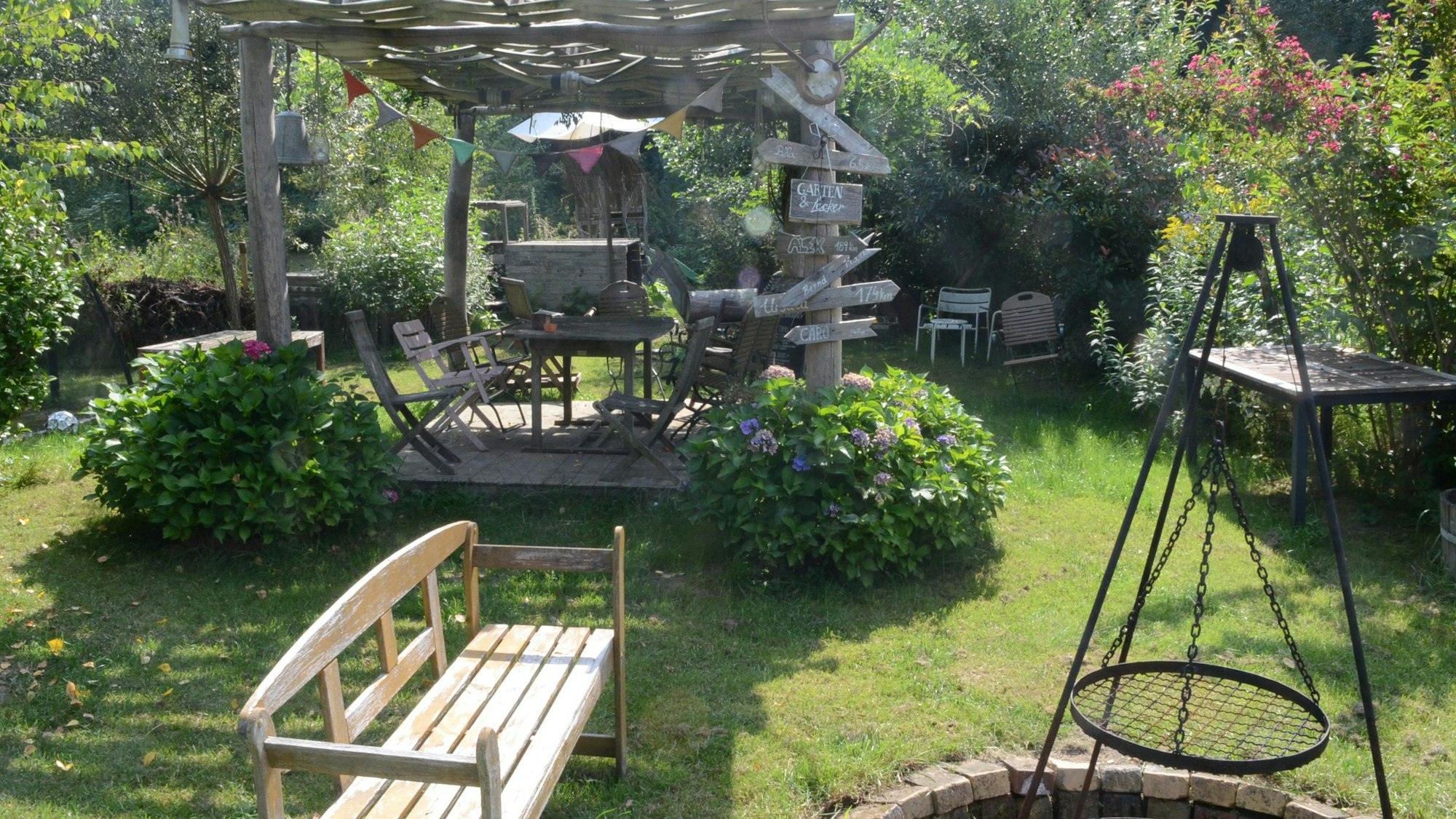 Blick auf einen Garten mit einer hölzernen Bank, einer Grillstelle und einer Pergola.