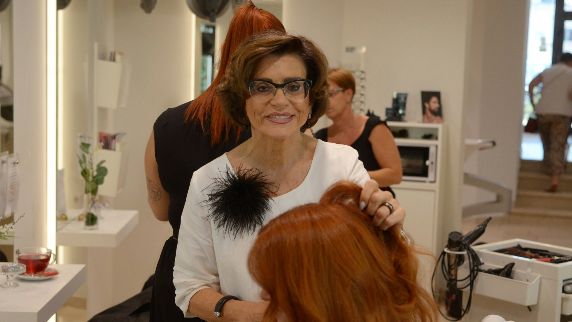 Martha Bungart bedient eine Kundin, die vor einem Spiegel sitzt. Im Hintergrund sind zwei ihrer Mitarbeiterinnen zu sehen.