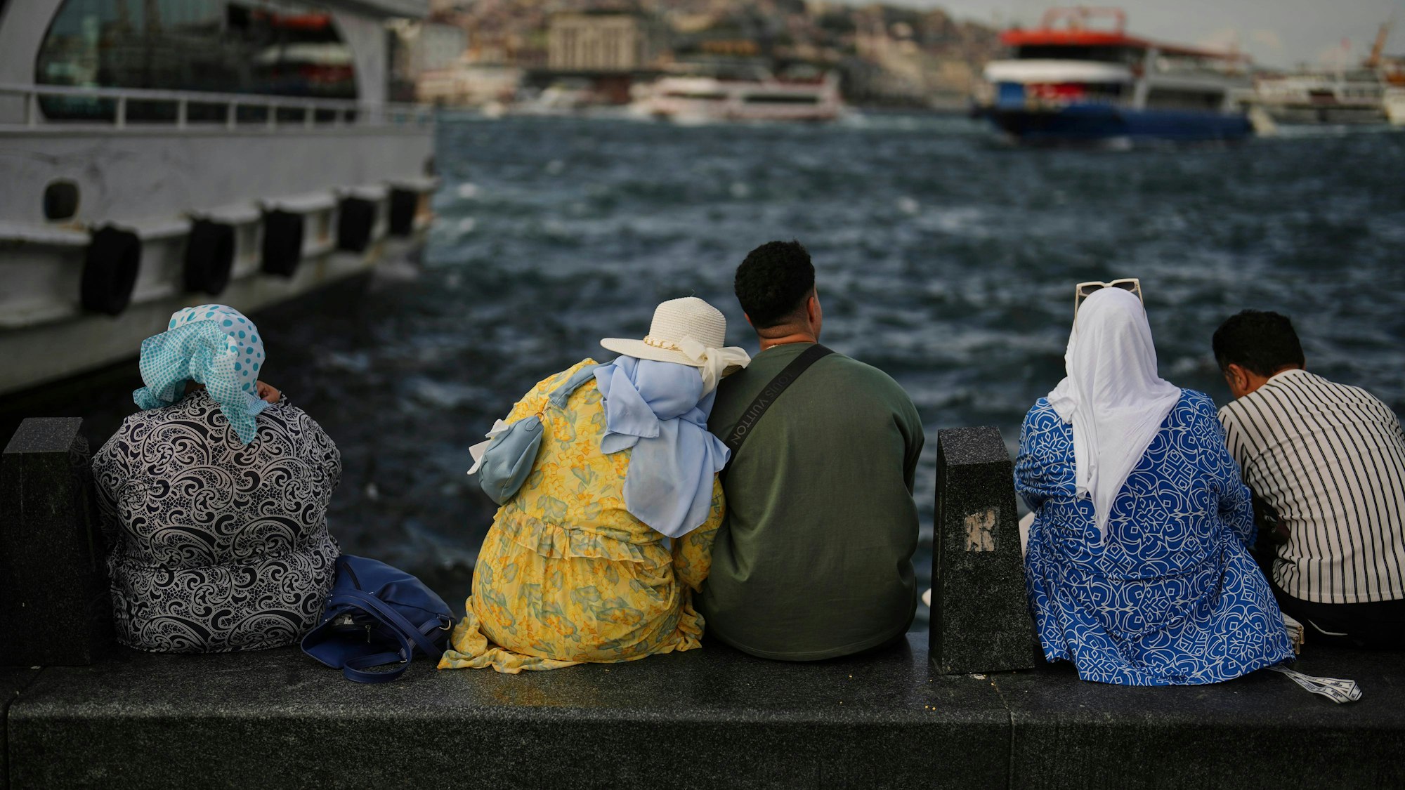 Istanbul: Menschen sitzen an der Eminonu-Promenade, während Fähren den Bosporus überqueren.