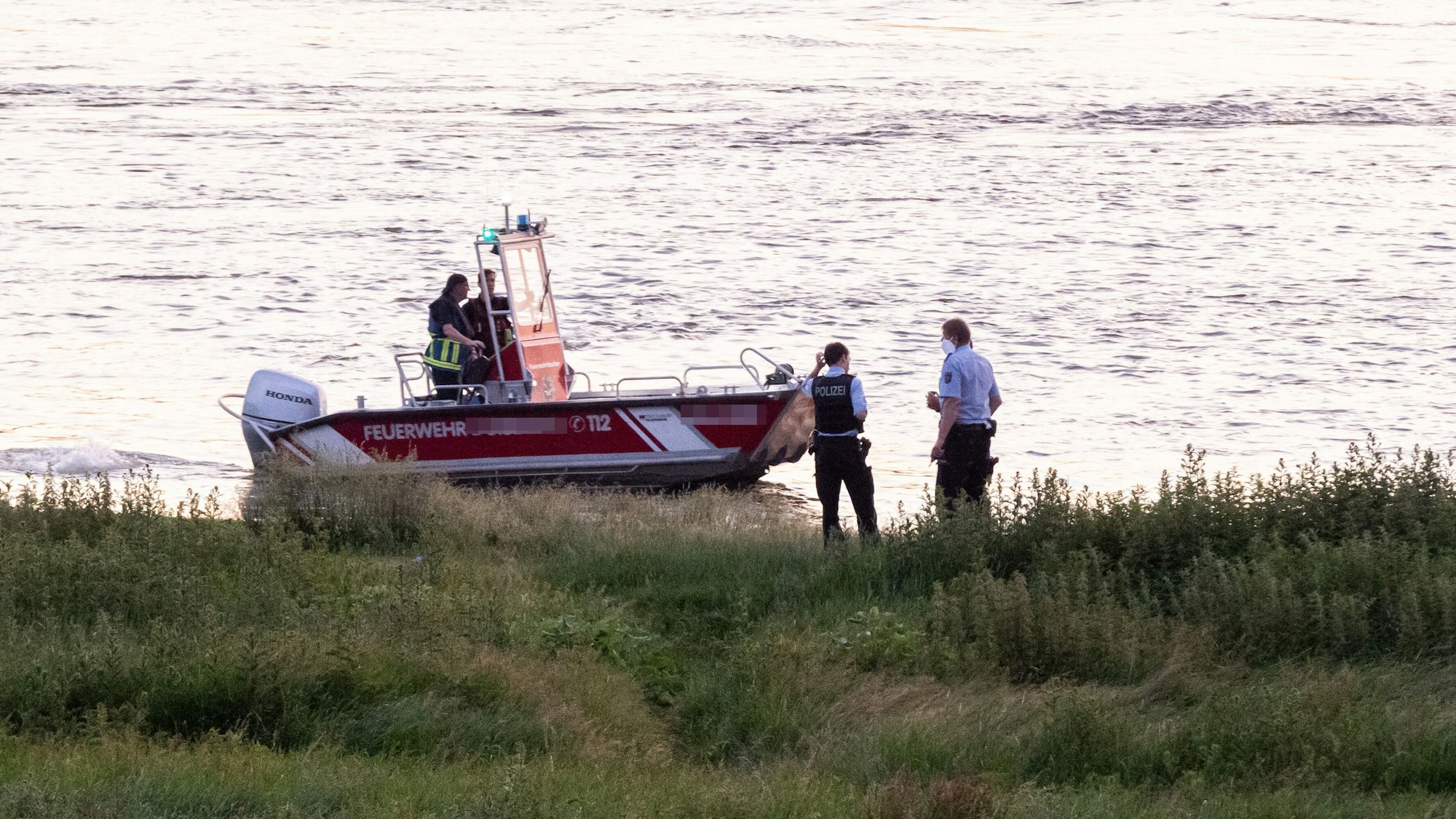 Einsatzkräfte der Polizei, Feuerwehr und DRLG arbeiten am Ufer des Rheins (Symbolfoto).