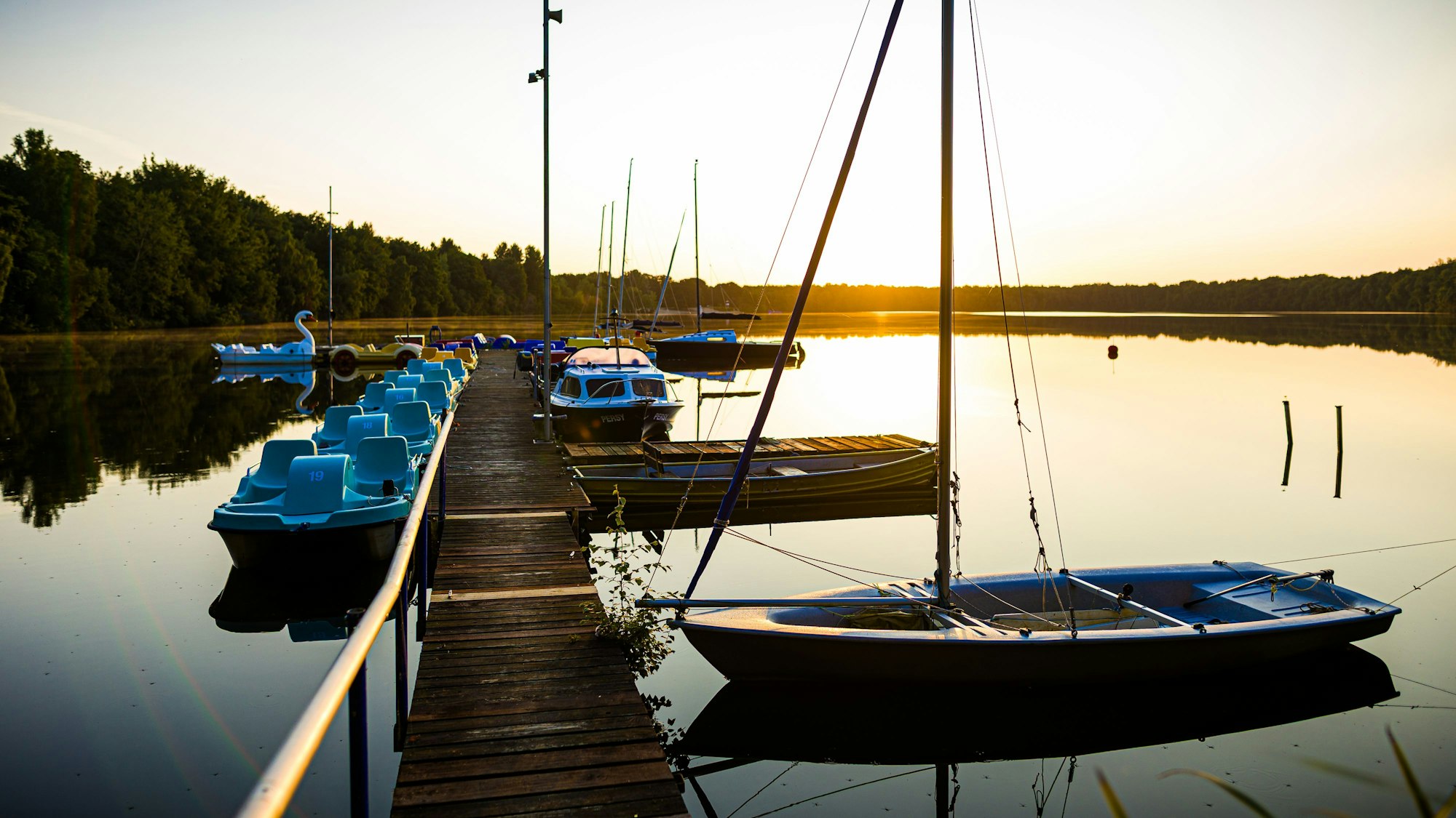 Kleine Boote liegen im Licht der aufgehenden Sonne an einem Steg im See.