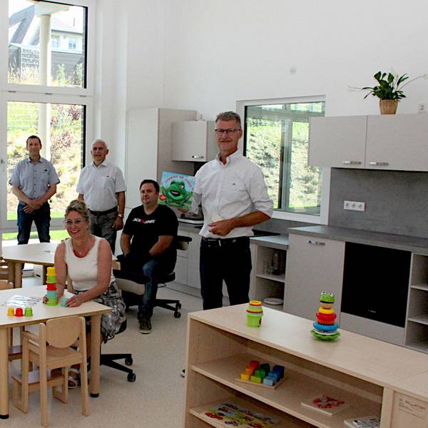 Eine Gruppe Männer und Frauen schaut sich die neuen Räume an, einige sitzen auf der Kinderstühlen.