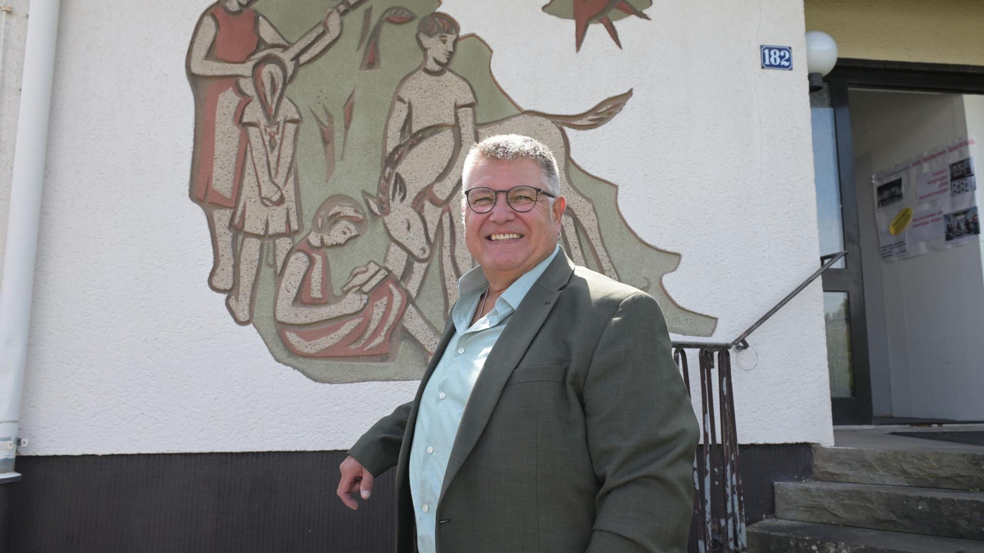Ein Mann steht vor einer Hausfassade mit einem großen Wandbild.