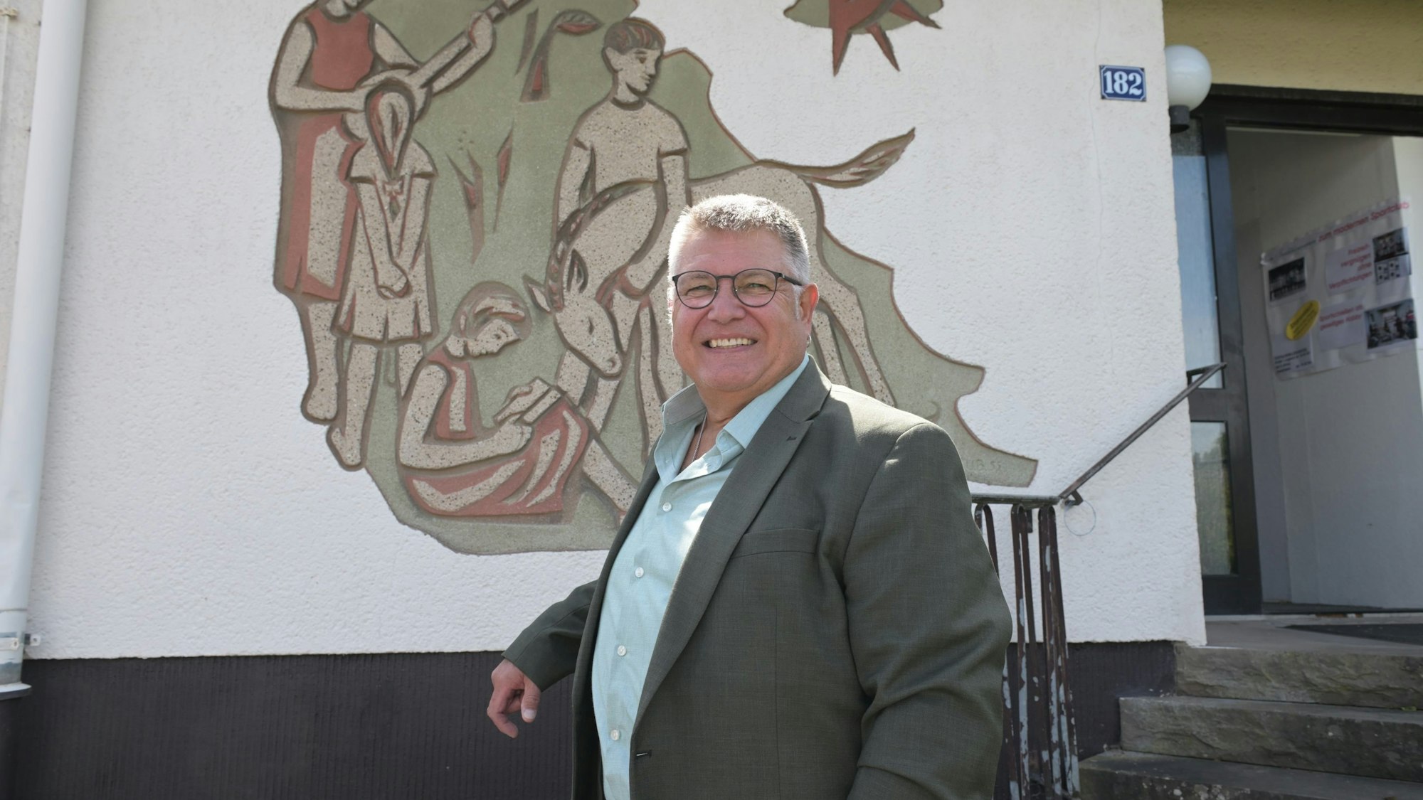 Ein Mann steht vor einer Hausfassade mit einem großen Wandbild.