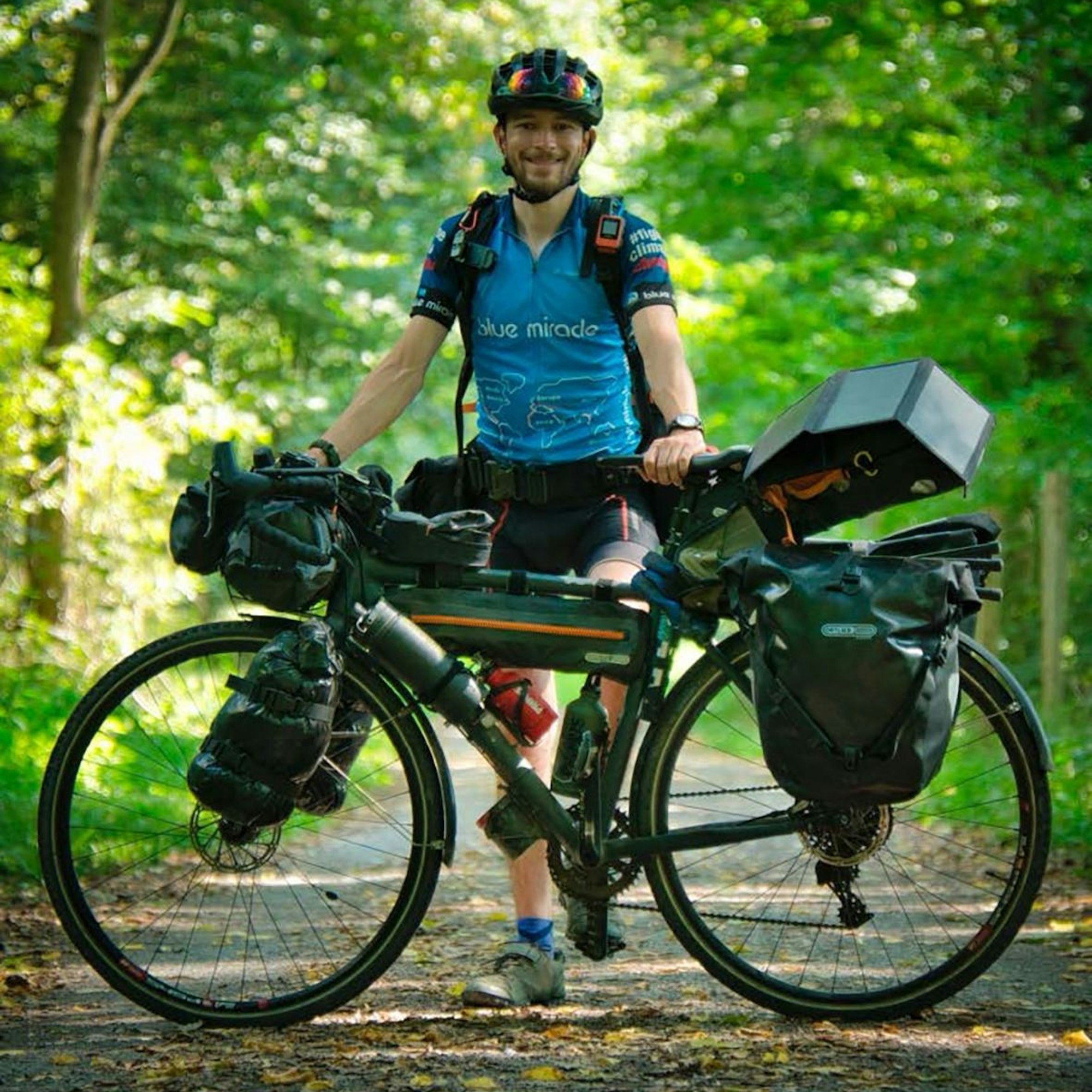Florian Berg steht in Fahrradkleidung hinter seinem vollgepackten Reiserad.