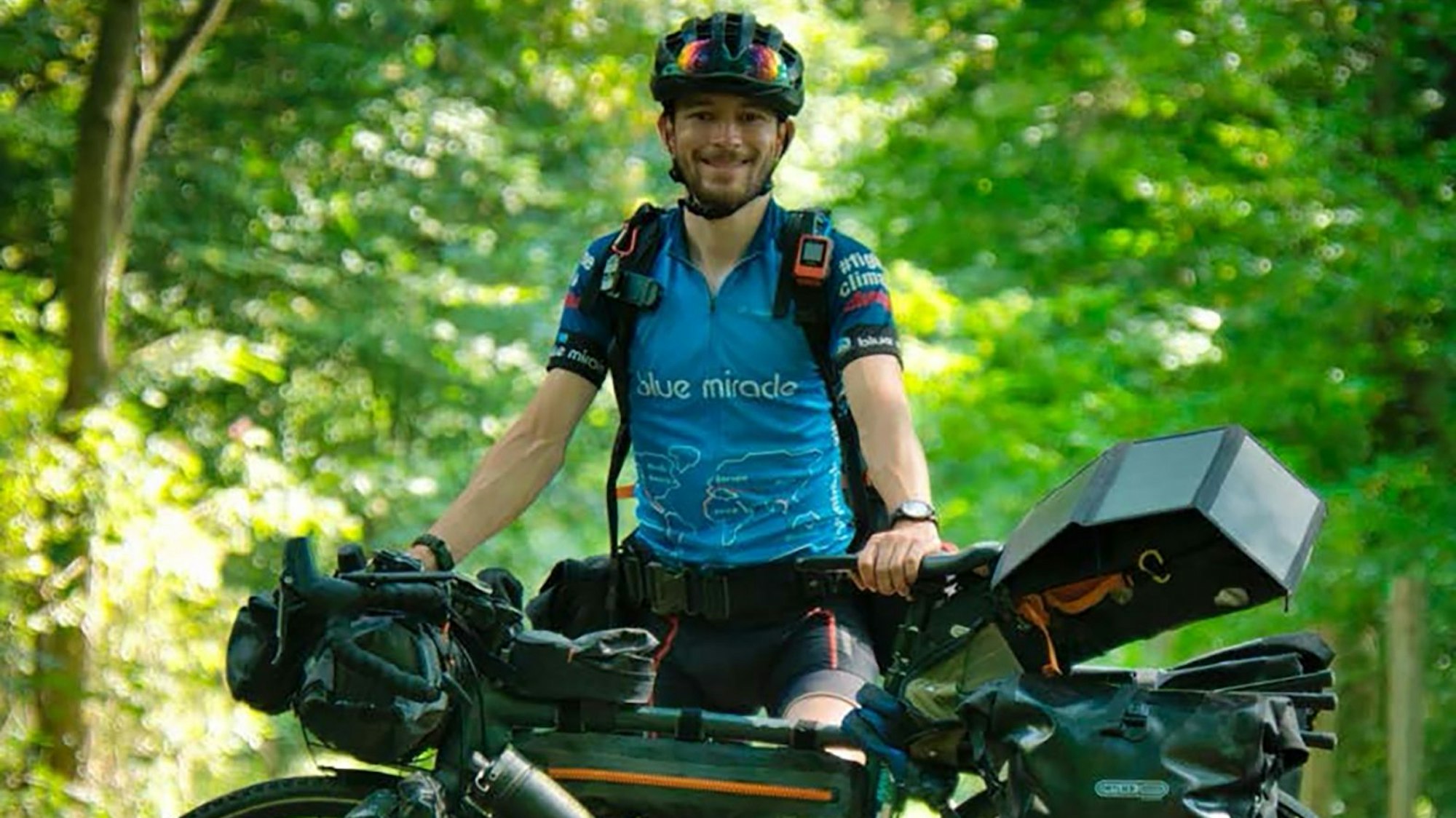 Florian Berg steht in Fahrradkleidung hinter seinem vollgepackten Reiserad.