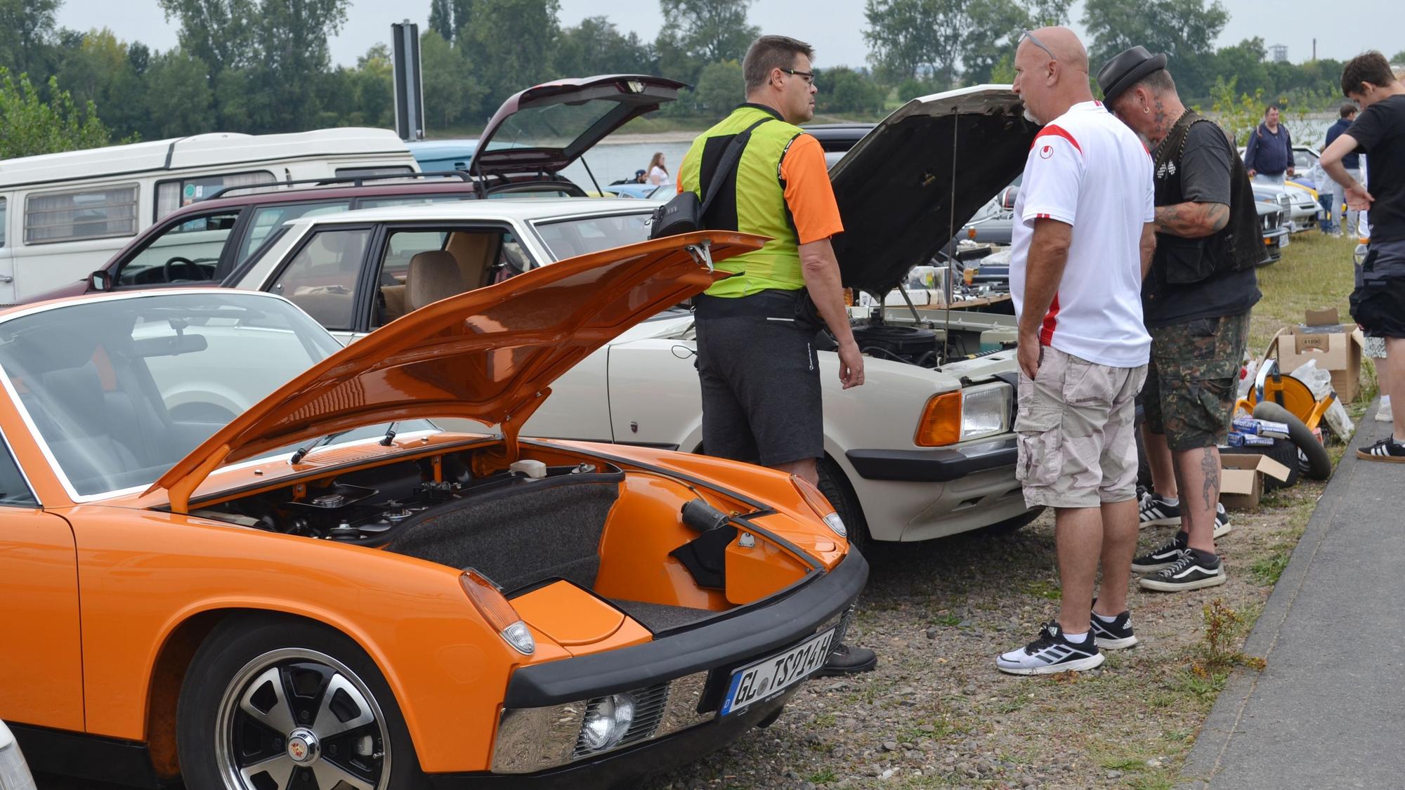 Drei Männer stehen vor Autos mit geöffneten Motorhauben.