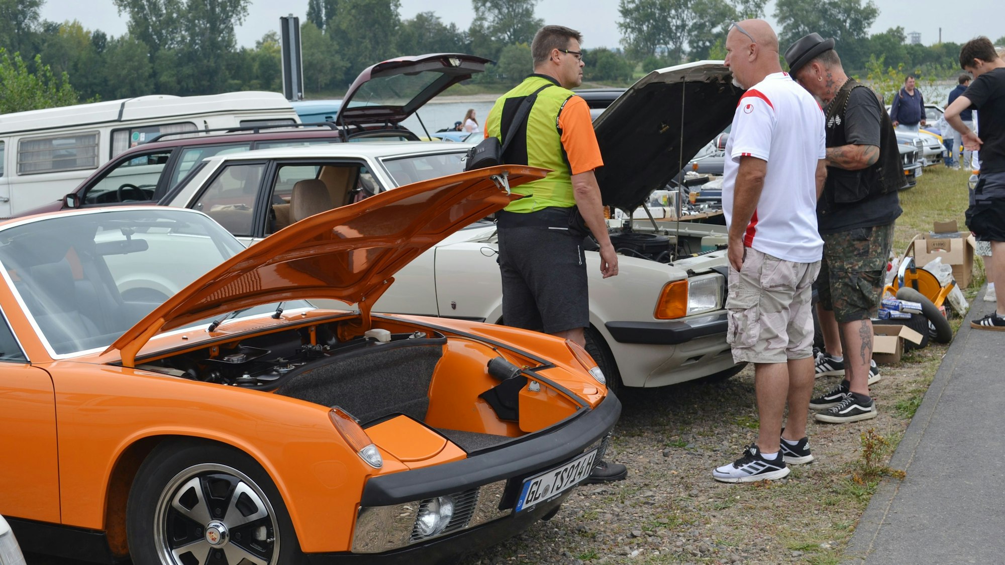 Drei Männer stehen vor Autos mit geöffneten Motorhauben.