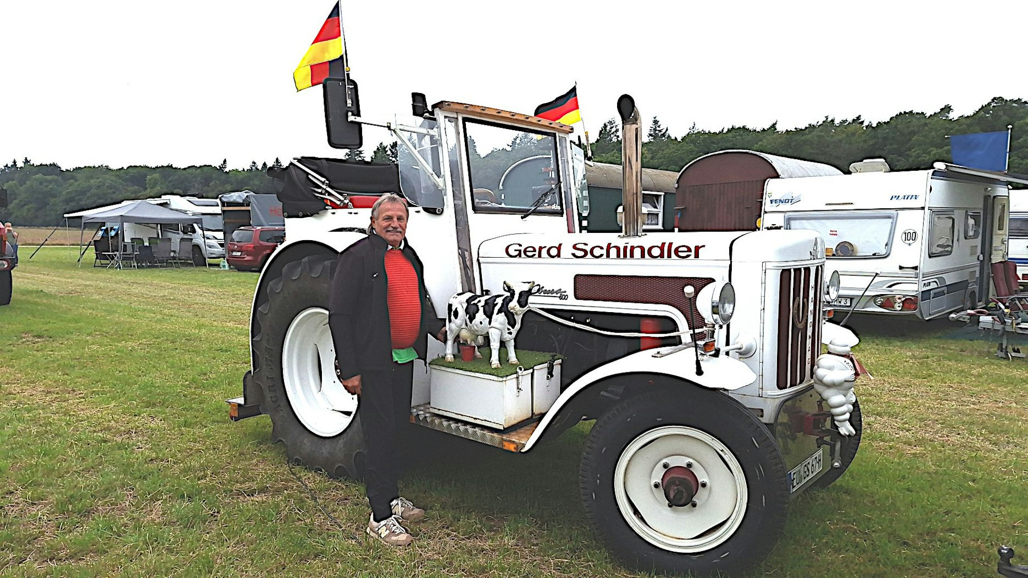 Gerd Schindler steht neben seinem umgebauten Hanomag. Auf dem Trittbrett gibt es ein kleines Stück Kunstrasen mit einer Kuhfigur.