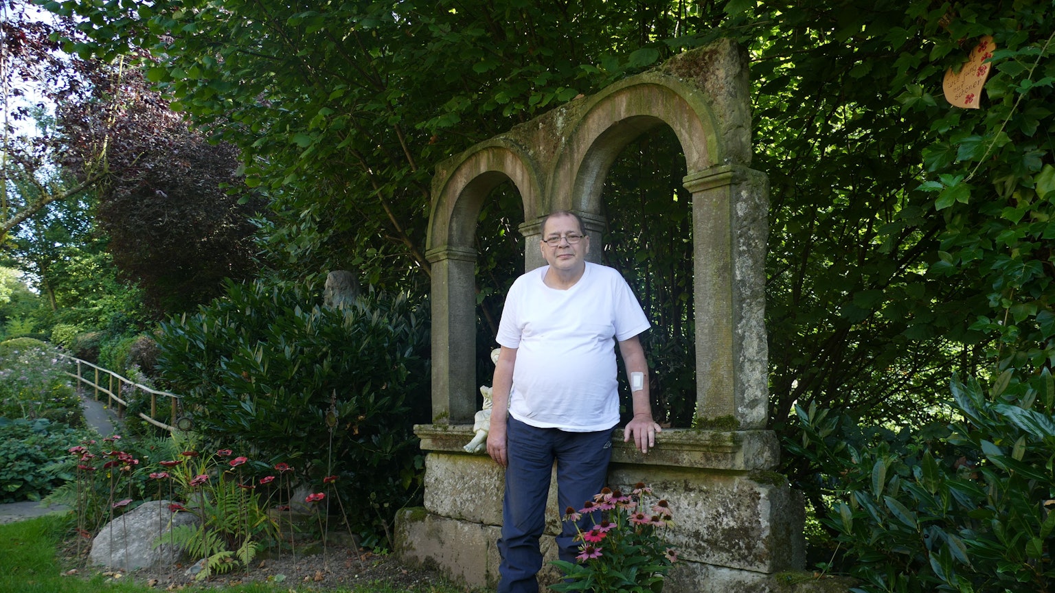 Ein Mann im weißen T-Shirt steht in einem Garten.
