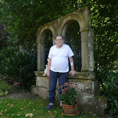 Ein Mann im weißen T-Shirt steht in einem Garten.