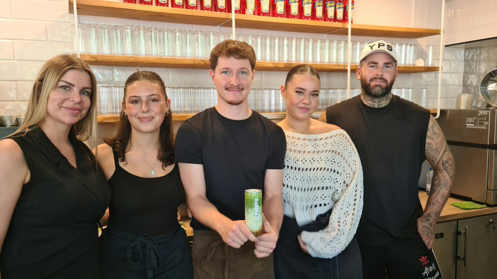 Fünf junge Leute stehen nebeneinander, einer hält eine Getränkedose mit dem Aufdruck Impi. Darin ist ein grünes Matcha-Getränk.