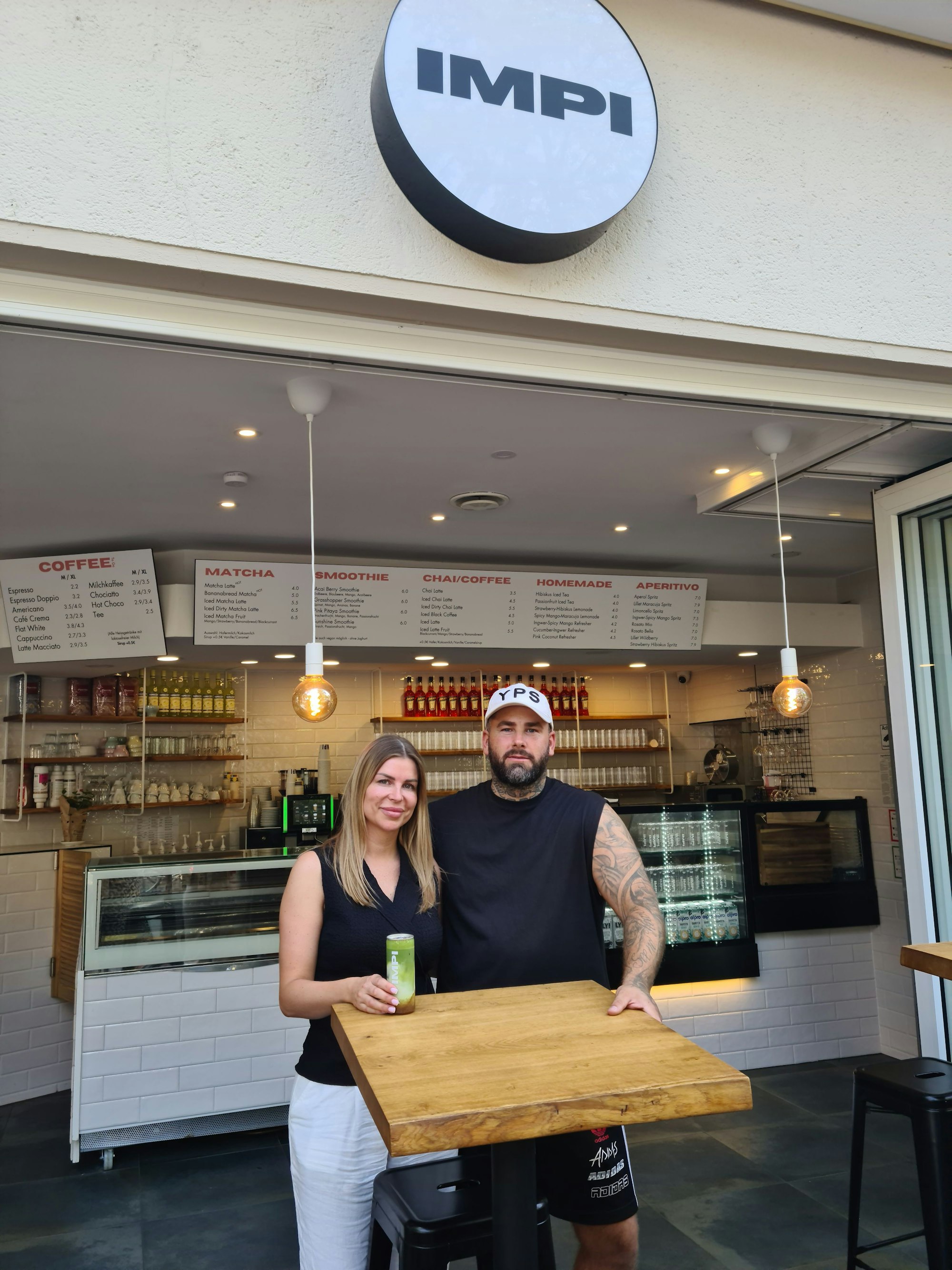 Ein Mann und eine Frau sitzen vor der geöffneten Fensterfront eines kleinen Cafés.
