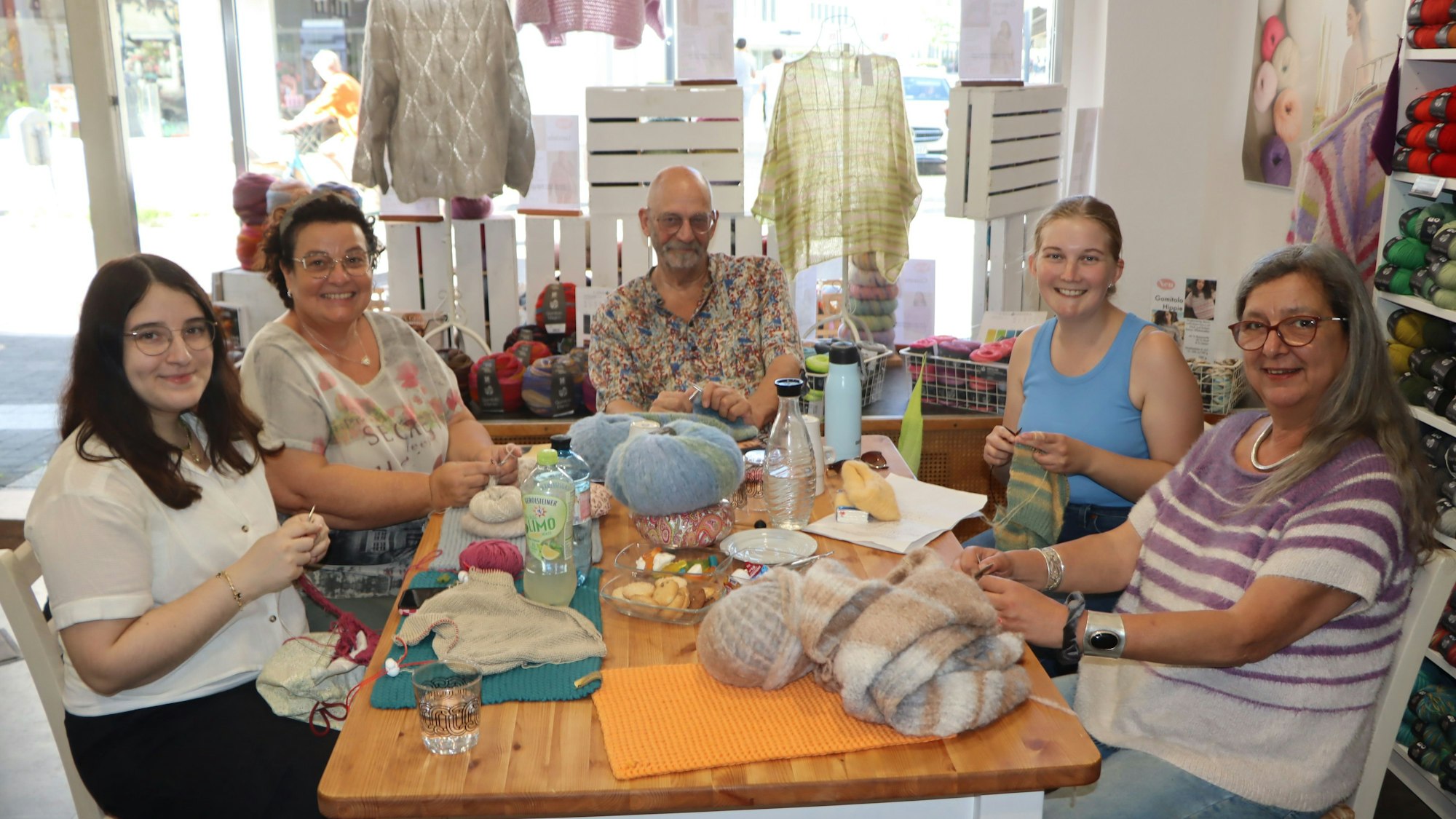 Vier Frauen und ein Mann sitzen an einem Tisch und stricken.