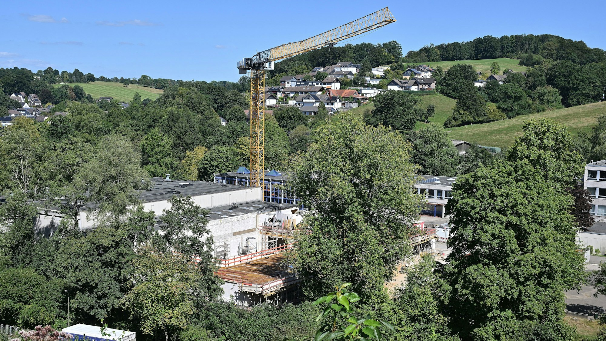 Ein großer Kran steht über unfertigen Rohbauten in einem grünen Tal.