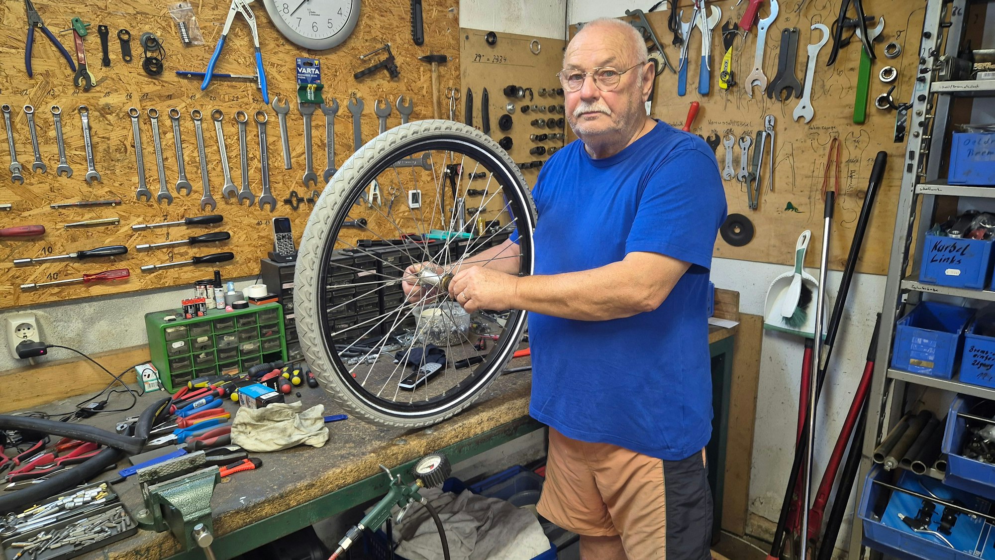 Ein Mann steht in der Werkstatt seines Fahrradgeschäfts und hält einen Reifen in den Händen.